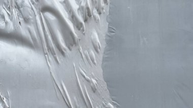 Düzensiz kırışıklıklar ve yükseltilmiş desenlerle pürüzsüz gri bir yüzeye yakın çekim, esnetilmiş plastik ya da kaplanmış maddeye benzer, soyut bir doku oluşturur.