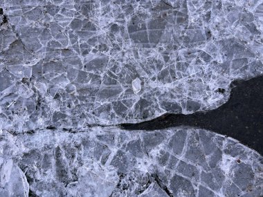 Kırık buz parçalarının yakın plan çizgileri ve sivri kenarları koyu bir arkaplan üzerinde beyaz ve gri tonlarında soyut bir model oluşturur..