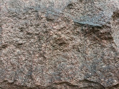 Kaba bir taş yüzeyin, doğal düzensiz dokusu ve gri ve kahverengi tonlarıyla yakın plan, kırsal bir arkaplan için ayrıntılı mineral desenlerini gösterir..