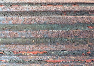 Paslı, kıvrımlı metal bir yüzeye yakın plan kırmızı, turuncu ve yeşil tonlarda soyulmuş boya, aşınmayı ve yıpranmış dokuyu gösteriyor..