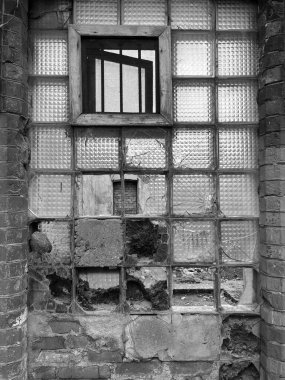 Cam bloklardan oluşan bir duvar ve ortasında ahşap çerçeveli bir pencere var. Terk edilmiş bir binada mimari bozulmayı ve dokuyu gösteren cesur bir şehir manzarası..