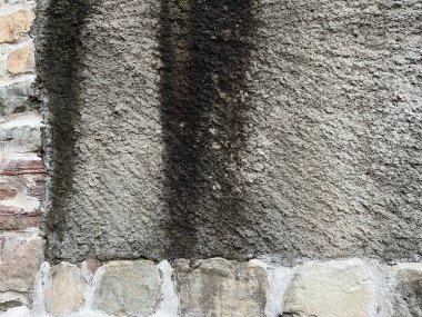 Eskimiş ve yıpranmış mimari ayrıntıları gösteren, koyu dikey lekeleri ve düzensiz taş blokların alt kısımlarına sahip kaba dokulu bir duvara yakın plan..