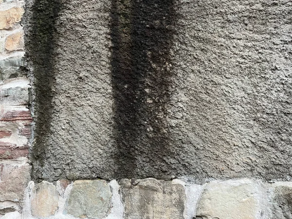 Eskimiş ve yıpranmış mimari ayrıntıları gösteren, koyu dikey lekeleri ve düzensiz taş blokların alt kısımlarına sahip kaba dokulu bir duvara yakın plan..