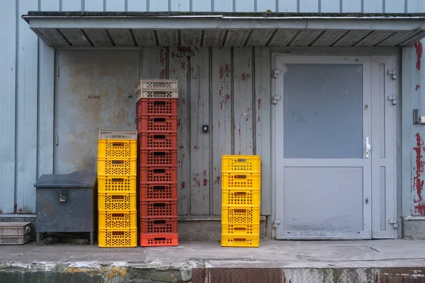 Sarı ve kırmızı plastik sandıklar eski bir endüstriyel kapı girişinin yanında. Boya soymak ve yıpranmış yüzeyler yaş ve günlük kullanım hissi katar..