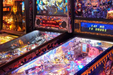 Renkli arka cam çizimleri ve parlayan oyun alanlarıyla bir atari salonunda birkaç aydınlatma tilt makinesi sıraya dizildi. Çerçeveyi parlak elektronik görüntüler, kontrol panelleri ve dekoratif grafikler doldurur.