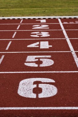 Close-up of white numbers on a red tartan running track lanes at athletic stadium