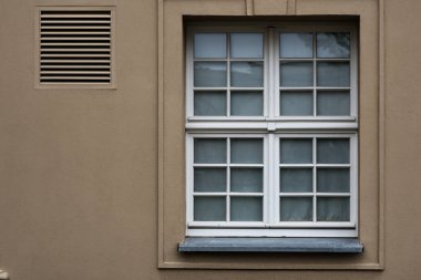 Havalandırmalı bej bir binanın ön cephesinde klasik beyaz pencere çerçevesi. Konut duvarının mimari ayrıntıları, dış tasarım ve gayrimenkul kavramı