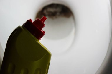 Klozet kapağına kırmızı açılı bir hortumla sarı bir temizleme şişesinin yakın çekimi kahverengi mineral birikimini gösteriyor, alçalmayı ve leke çıkarmayı gösteriyor..