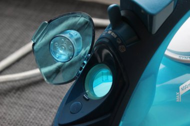 Buharlı demir su deposunun kapağı açık ve doldurulmaya hazır yakın görüntüsü. Mavi şeffaf plastik, ev aletleri detayı.