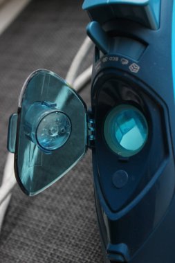 Buharlı demir su deposunun kapağı açık ve doldurulmaya hazır yakın görüntüsü. Mavi şeffaf plastik, ev aletleri detayı.