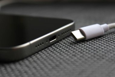 USB-C kablosu dokuma yüzeyinde USB-C portu olan bir akıllı telefonun yanında örülmüş, şarj konsepti.