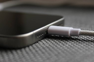 Örgülü bir USB-C kablosunun yakın plan görüntüsü gri örülmüş bir yüzeyde modern bir akıllı telefona güvenli bir şekilde takıldı. Kopyalama alanı olan temiz teknik detay.
