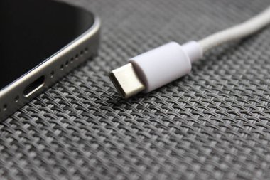 USB-C kablosu dokuma yüzeyinde USB-C portu olan bir akıllı telefonun yanında örülmüş, şarj konsepti.