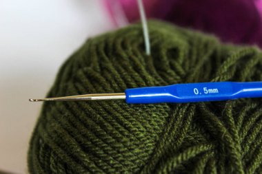 Mavi saplı 0.5 mm çelik örgü kancası zeytin yumağının üzerinde duruyor. Hassas dantel ve ince işçilik araçları kavramı.