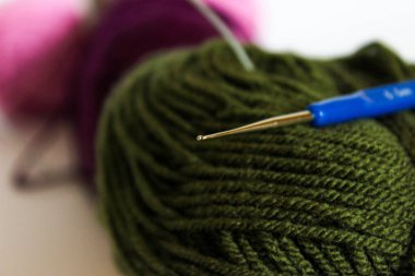 Mavi saplı 0.5 mm çelik örgü kancası zeytin yumağının üzerinde duruyor. Hassas dantel ve ince işçilik araçları kavramı.