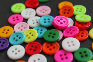 Koyu bir yüzeye gevşek bir şekilde yerleştirilmiş çeşitli renkli dikiş düğmeleri. Tekstil ve DIY için temiz zanaat kavramı.