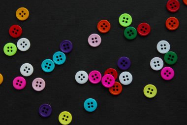 Siyah kağıda serpiştirilmiş renkli düğmeler, negatif boşluklu oyuncu bir şablon oluşturuyor.