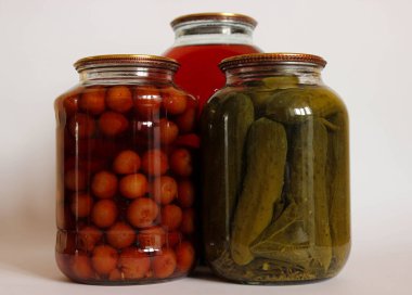 Üç büyük cam kavanoz. Meyve kompostosu, salatalık turşusu ve beyaz arka planda sade bir yaşam için düzenlenmiş başka bir komposto..