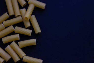Pişmemiş rigatoni karanlık bir yüzeyin köşesine saçılmış yemek tarifleri, menüler ya da posterler için uzun negatif alan bırakarak..