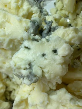 Kremsi dokuları ve mavi damarları gösteren parçalanmış mavi peynirin makro görünümü, gurme süt ürünleri arka planı.