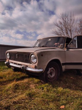 Bulutlu gökyüzünün altında çimlerin üzerine park etmiş yıpranmış Sovyet döneminden kalma bir sedan..