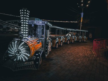 Parlak ışıklı bir festival treni, yeşil ve sarı ışıklarla parlayan gece park halinde duruyor. tatil atmosferi.