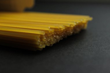 Koyu bir yüzeye yerleştirilmiş pişmemiş makarna yığını. Kuru makarnanın dokusunu, şeklini ve sarı rengini gösteren yakın çekim görüntüsü.