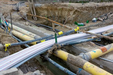 Açıkta toprak ve su bulunan bir inşaat alanındaki açık bir sipere uzanan bir yığın kanal ve büyük borular..