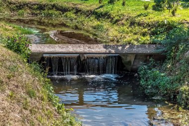 Ukrayna Romny, Sumy bölgesindeki Kozatska Prystan dinlenme tesisinde akan su ve yemyeşil bitki örtüsüne sahip beton şelale. Huzurlu doğal akış manzarası yansımaları ile