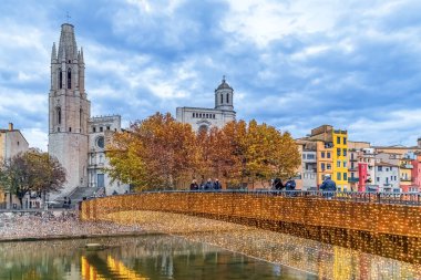 Girona 'daki Onyar Nehri' ne yansıyan Noel ışıklarıyla süslenmiş Aziz Feliu Köprüsü. Tarihsel Bazilika ve renkli evler sonbahar mevsiminde pitoresk şehir manzarası yaratıyor. Girona, İspanya - 27 Kasım 2021