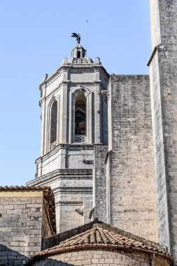 İspanya 'daki açık mavi gökyüzüne karşı Girona Katedrali' nin tepesinde melek heykeli olan taş çan kulesi. Ortaçağ mimarisinde antik taş duvarlar ve geleneksel teras kiremitlerinin yanında zarif sütunlar ve kemerli açıklıklar yer almaktadır.