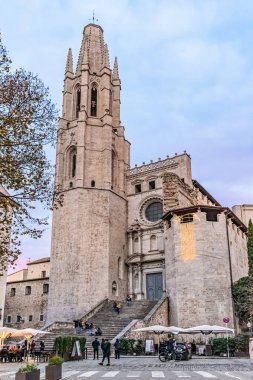 Alacakaranlıkta Girona 'daki Sant Feliu Bazilikası' nda Gotik çan kulesi ve büyük merdivenleri var. Ziyaretçiler merdivenlerde toplanırken, Noel süsleri tarihi kilise cephesini aydınlatıyor. Eski kasabada akşam atmosferi. Girona, İspanya - 27 Kasım 2021