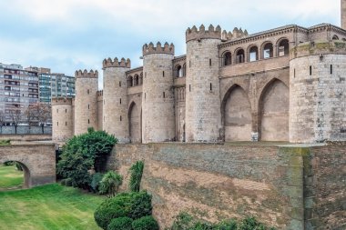 İspanya, Zaragoza 'daki Aljaferia Sarayı' nın görkemli manzarası. Bu ortaçağ İslam kalesinde bulutlu bir gökyüzünün altında taş savunma kuleleri ve antik takviye duvarları bulunuyor.
