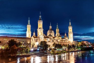 İspanya 'nın Zaragoza kentindeki koyu mavi gökyüzüne karşı Basilica del Pilar' ın gece görüşü. Katedral ışıkları Ebro Nehri 'nin sularını yansıtıyor.