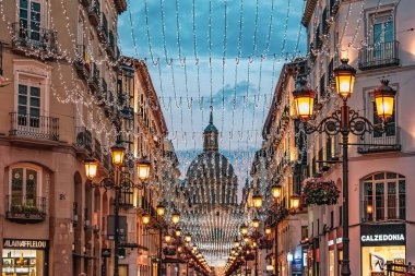 Alfonso I caddesindeki simetrik şehir perspektifi derin mavi bir alacakaranlık gökyüzünün altında. Tatil ışıklarını asmak tarihi katedral kubbesine doğru parlak bir tünel açar. Zaragoza, İspanya - 29 Kasım 2021
