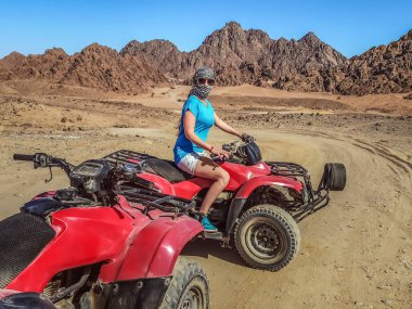 Mısır 'ın Sina Çölü' nde bir ATV 'nin önünde, arafatka giymiş yetişkin bir beyaz kız oturuyor. Sharm El Sheikh 'te turistler için ATV gezisi