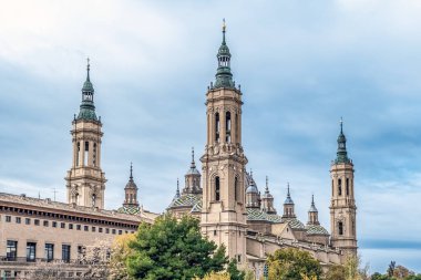 İspanya, Zaragoza 'da çok sayıda kulesi ve renkli kubbeleri olan Bazilika del Pilar' ın güzel yan manzarası. Bu simge yeşil ağaçlarla birlikte muhteşem bir barok mimari sergiliyor.