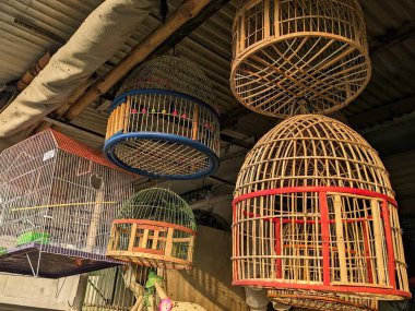 Geleneksel el yapımı bambu kuş kafesleri gri metal çatılı kahverengi arka planda asılı.