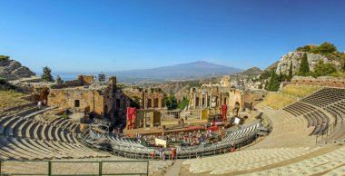 Taormina, Sicilya, İtalya 'daki antik Yunan tiyatrosunun panoramik görüntüsü. Tarihi taş kalıntıları, pitoresk mimari ve açık mavi gökyüzünün altındaki Etna Dağı 'nın nefes kesici manzarası..