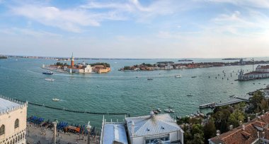 Temiz bir gökyüzü altında tarihi adalar, tekneler ve kıyı mimarisinin yer aldığı Venedik Gölünün geniş panoramik manzarası. Bu manzara Venedik, İtalya 'nın ikonik simgeler, sakin sular ve hareketli turistik yerleri de içeren güzelliğini yansıtır..
