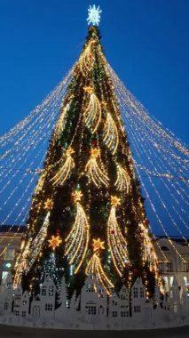 Gece meydanında parlak ışıklar ve yıldızlarla parıldayan güzel dekore edilmiş bir Noel ağacının göz kamaştırıcı manzarası. Tatil, kutlama ve kış büyüsünün mükemmel atmosferi..