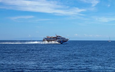 Modern hidrofolyo feribotu, güneşli bir günde beyaz bir uyanış bırakarak mavi deniz suyunda hızla süzülür. Seyahat, ulaşım, yaz tatili ve deniz macerası konsepti.