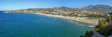 Canlı bir İtalyan sahil şehrinin panoramik manzarası kumlu sahil, turkuaz deniz ve dağ zeminiyle. Tatil, turizm, manzara, rahatlama ve seyahat temaları için mükemmel bir yer..