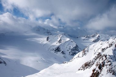Yüksek karla kaplı dağların panoramik kış manzarası ve kasvetli bulutların altındaki engin buzul vadisi. Soğuk yaban hayat, macera yolculuğu, iklim ve doğa kavramı.