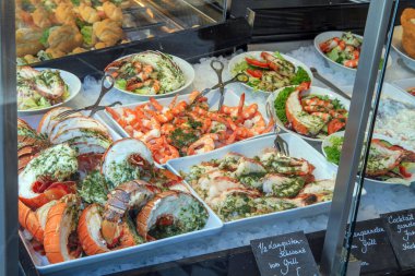 Istakoz, karides ve buzda kabuklu deniz ürünleri sergilenen soğuk bir vitrinde taze pişmiş deniz ürünleri seçimi, otlar ve salata garnitürüyle servis ediliyor. Piyasa gıda perakende kavramı.