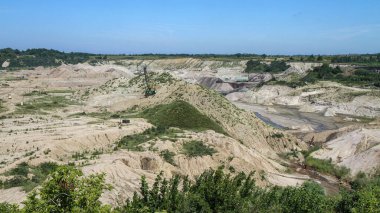 Kum ve çakıl ocağı geniş görüş alanı kazıcı mekanizmaları, enkaz yığınları ve engebeli arazi mavi gökyüzü altında. Endüstri, çıkarma ve çevre kavramı.