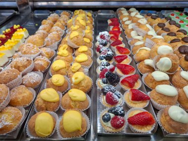 Fırın vitrininde renkli hamur işleri ve kremalı, çikolatalı ve meyveli mini meyveli turtalar. Tatlı görüntüsü, tatlı ikram çeşitliliği, pastane arka planı.