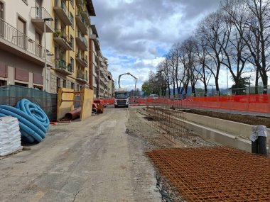 Siperli, demir çubuklu, borulu ve turuncu bariyerlerin arkasındaki beton kamyonlu şehir caddesi tadilatı. Altyapı güncellemesi ve kamu çalışmaları.