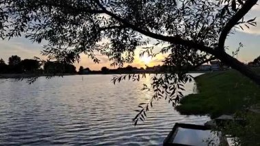 Altın yansımalı, sakin sulu ve huzurlu manzaralı bir gölde güzel bir gün batımı. Sinema projeleri, doğa videoları, rahatlama görselleri ve arka plan ambiyansı için mükemmel..