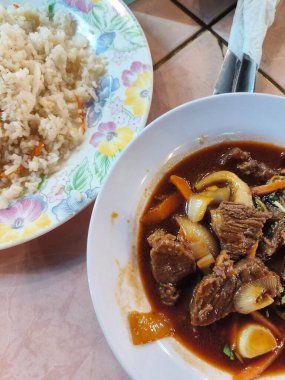 Bu resimde geleneksel Hainese usulü sığır kuyruğu güveci ve yanında bir tabak pilav, muhtemelen kızarmış pirinç veya tereyağlı pilav servis ediliyor..